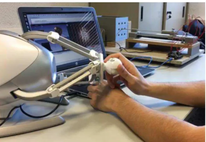 Fig. 3. Novint Falcon, in foreground, with the robotic system and the phantom in background  A proof of concept has been carried out in the  “Surgical Simulation and Planning”  course of the fourth year of the Bachelor in Biomedical Engineering of the UPM