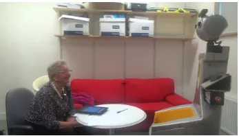 Fig. 2. Focused experiment in a controlled setting. The elderly participant is sitting infront of the robot, while the tablet is detached and placed on the table easy accessibleby the user.