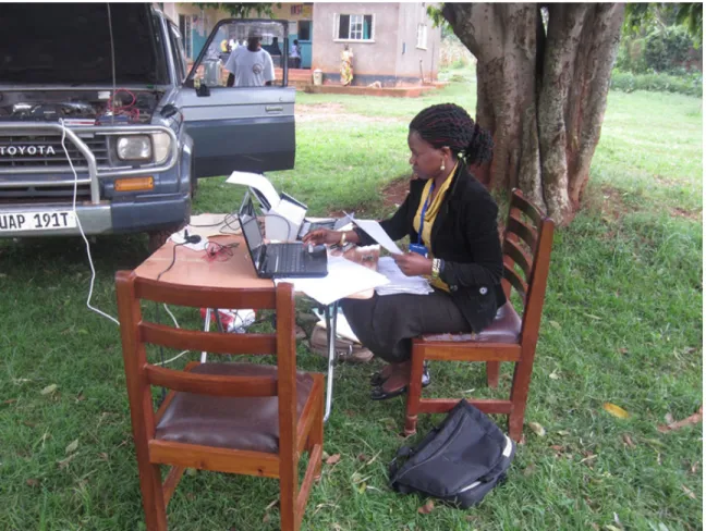 Figure 2. Field data collection workspace powered by car battery. (Stellah Kayongo using  folding table, laptop, and scanner in Bowa, Uganda, August 2012.) 