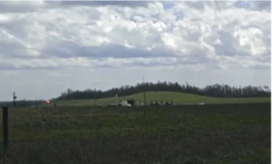 Figure 11. View of a drill site from atop an access road. The bright orange flare of a gas well  can be seen on the left side of the photo