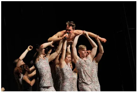 Figure 2: From Kill Your Darlingshis shirt and “supported”, or carried away, by the athletic choir representing : The actor Fabian Hinrichs stripped off the capitalist network, in dollar bill clothing
