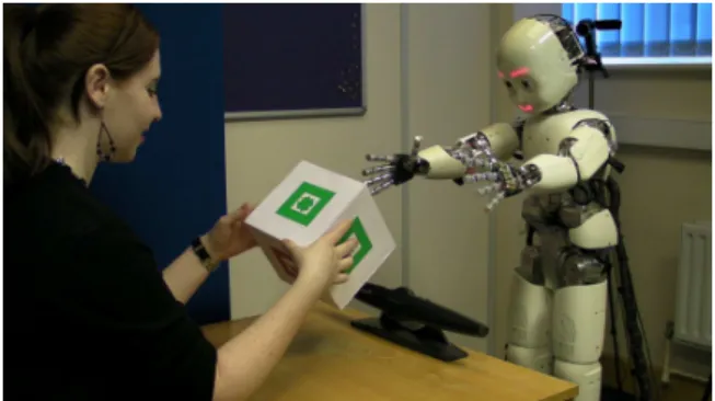 Figure 1. An experiment with the iCub robot. The participant is asked to teach iCub the words for shapes and colors on the box, speaking as if the robot were a small child