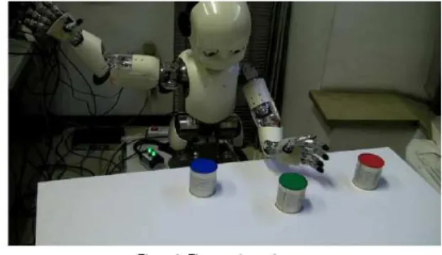 Figure 2. The set up for iCub for experiments described in Section 2.1. The robot is trained through a trial-and-error process to respond to sentences such as “reach the green object”